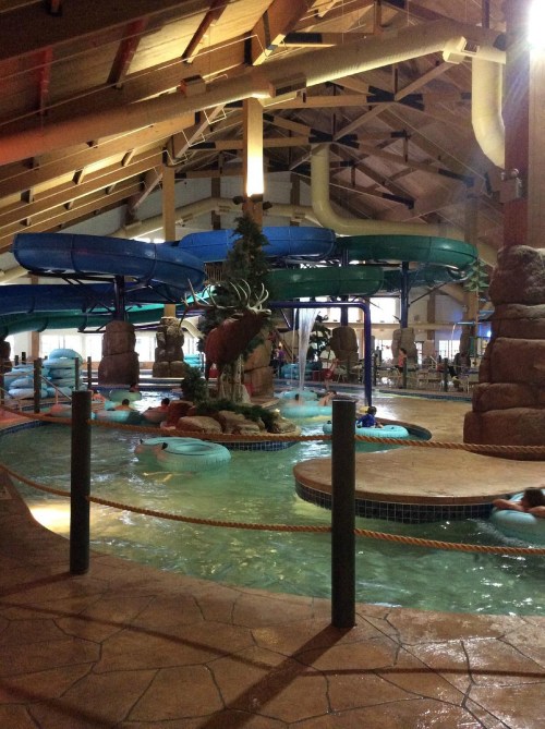 Indoor water park featuring water slides, a lazy river, and a tropical-themed decor with rocks and greenery.