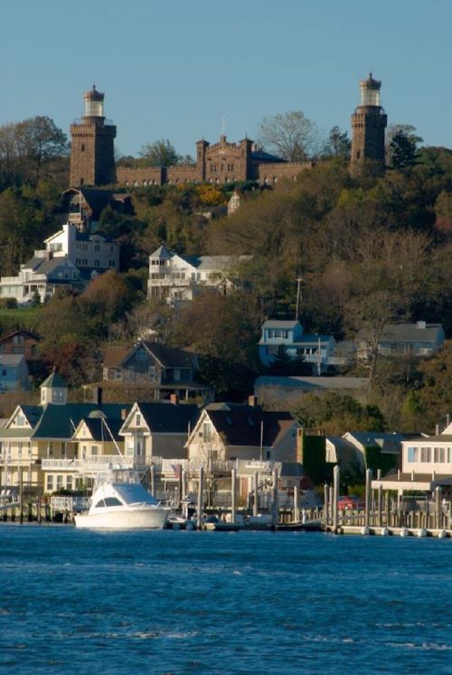A scenic view of a waterfront with a boat, houses, and a hilltop castle-like structure in the background.