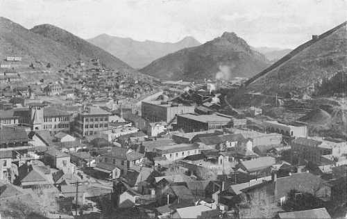 A historic black-and-white view of a mountainous town with buildings and factories nestled in the valley.