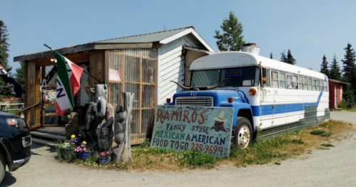 A blue and white bus parked beside a rustic building with a sign for "Ramiro's Family Style Mexican American Food."