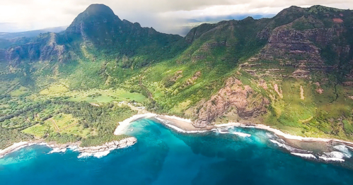 Aerial view of lush green mountains meeting a turquoise coastline with gentle waves lapping at the shore.