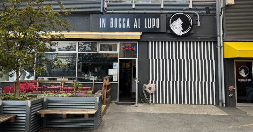 Exterior of a restaurant named "In Bocca Al Lupo," featuring an open sign and outdoor seating.