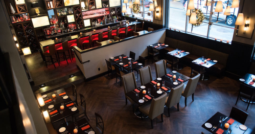 A modern restaurant interior with tables set for dining and a stylish bar in the background. Warm lighting creates a cozy atmosphere.