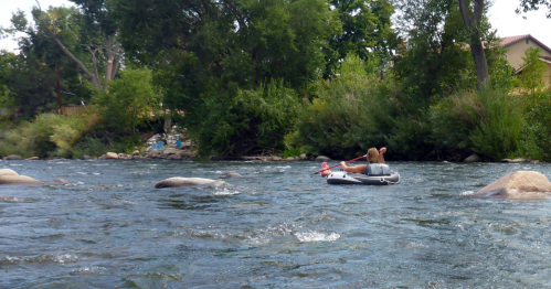 A person floats on a river in an inflatable raft, surrounded by rocks and lush greenery.