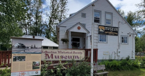 Exterior of the Talkeetna Historical Society Museum, featuring a sign and informational display about the old schoolhouse.