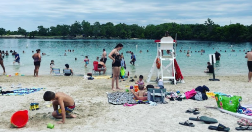 A busy beach scene with people swimming, sunbathing, and children playing in the sand near a lifeguard station.