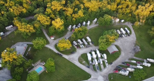 Aerial view of a campground with RVs, surrounded by trees with autumn foliage and a swimming pool nearby.
