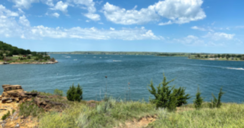 A scenic view of a lake surrounded by green hills and blue skies with fluffy clouds.