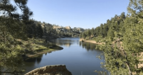 A serene lake surrounded by trees and rocky hills under a clear blue sky.