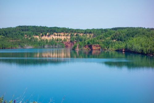 A serene lake surrounded by lush greenery and steep, rocky cliffs under a clear blue sky.