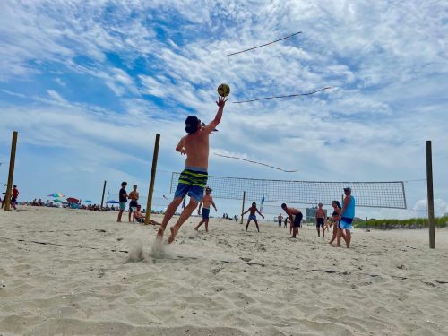 A group of people playing beach volleyball on a sunny day, with colorful ribbons flying in the background.