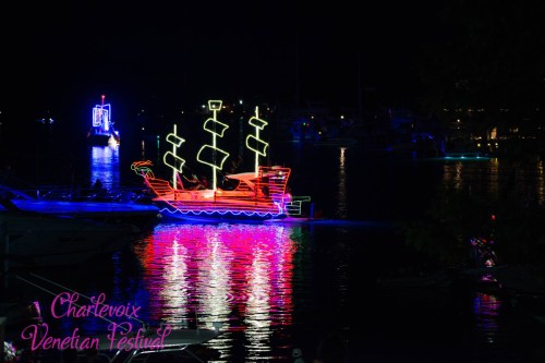 Colorful illuminated boats at night during the Charlevoix Venetian Festival, reflecting on the water.