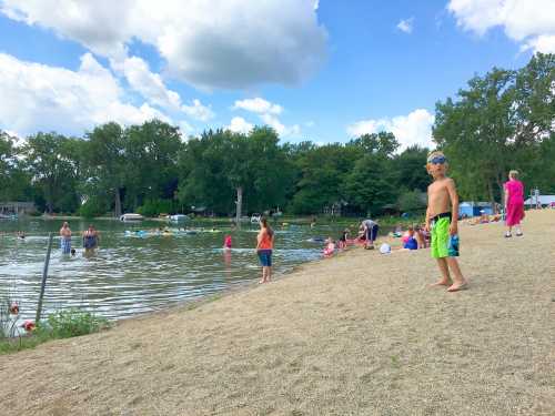 A sandy beach by a lake with people swimming, playing, and relaxing under a partly cloudy sky. A child stands in the foreground.