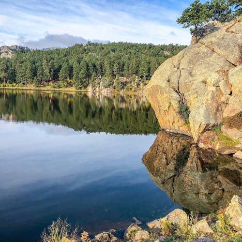 A serene lake surrounded by trees and rocky formations, reflecting the landscape in calm waters.