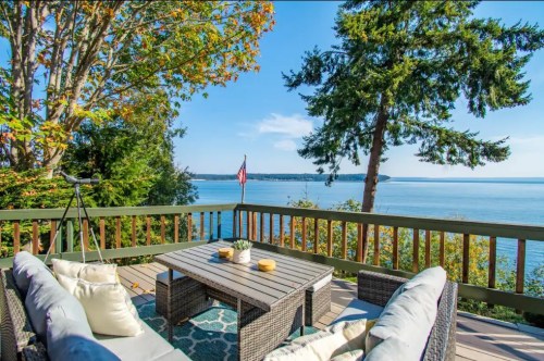 A scenic view from a deck overlooking a calm body of water, surrounded by trees and a clear blue sky.