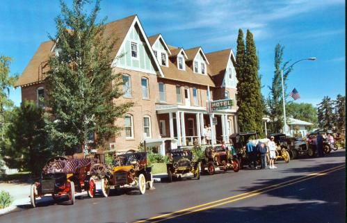 A historic hotel with a row of vintage cars parked in front, under a clear blue sky.