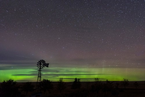 A windmill silhouetted against a starry sky with green auroras illuminating the horizon.