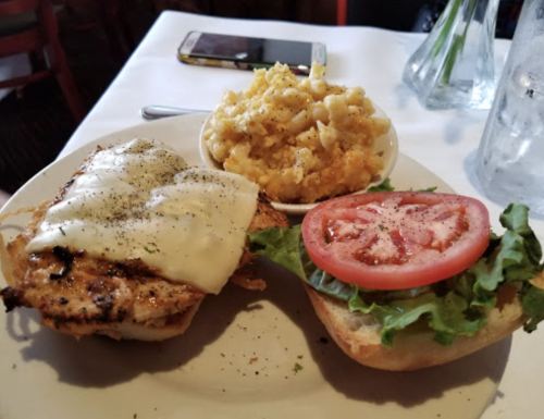 A plate with a grilled chicken sandwich topped with cheese, lettuce, and tomato, alongside a bowl of macaroni and cheese.