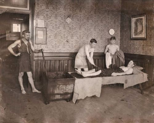 Historical photo of four men in a spa setting, with one receiving a treatment while others assist.