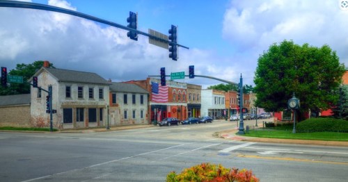A small town intersection with historic buildings, traffic lights, and an American flag displayed on a nearby structure.