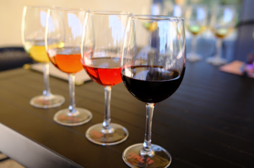 Four wine glasses filled with different colored wines, arranged on a table with more glasses in the background.