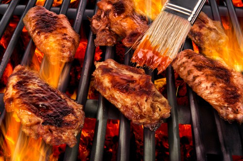 Grilled chicken wings on a barbecue, with flames and a brush applying sauce.