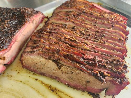 Sliced smoked brisket with a dark, crispy crust on a cutting board.