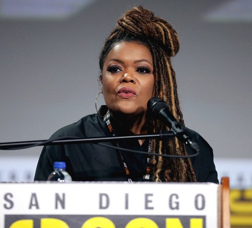 A woman with long, braided hair speaks into a microphone at a panel during San Diego Comic-Con.