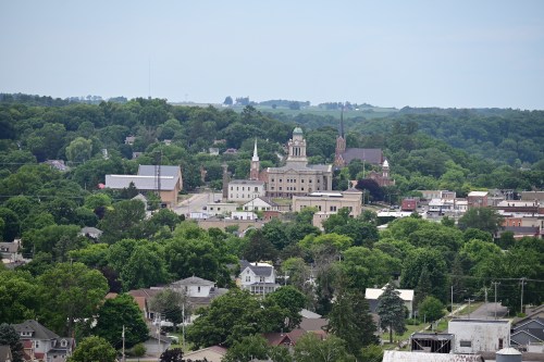 A panoramic view of a small town surrounded by lush greenery, featuring historic buildings and a church steeple.