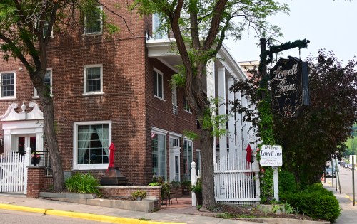 A charming brick inn with a sign, surrounded by trees and a white picket fence, inviting guests to enter.