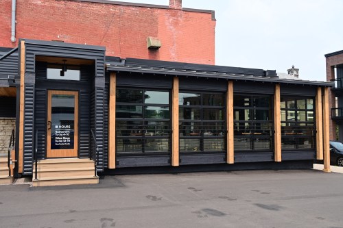Modern building exterior with large glass windows and wooden accents, featuring a sign with business hours.