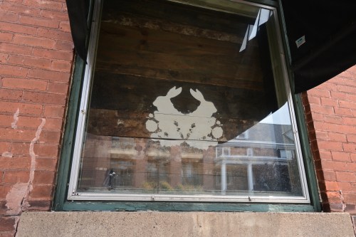 A window with a faded crab silhouette against a rustic wooden background.