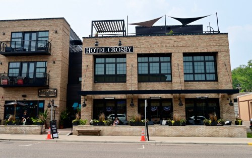 Exterior view of Hotel Crosby, a brick building with large windows, outdoor seating, and decorative awnings.