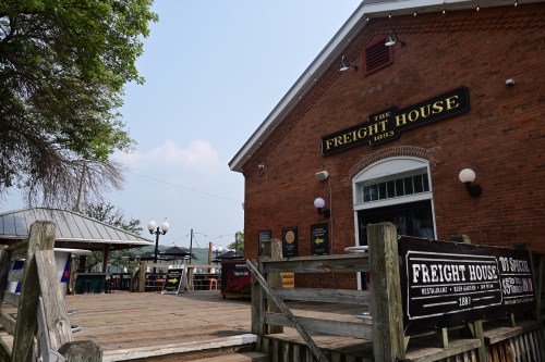 Exterior of The Freight House restaurant, featuring a brick facade and wooden deck, under a clear blue sky.