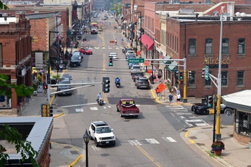 A busy street scene with cars, pedestrians, and shops, featuring traffic lights and roadwork signs in a small town.
