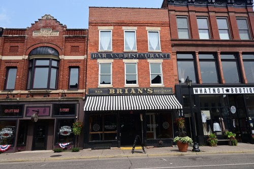 Historic brick building featuring "Brian's Restaurant" with striped awning, flanked by shops on a city street.