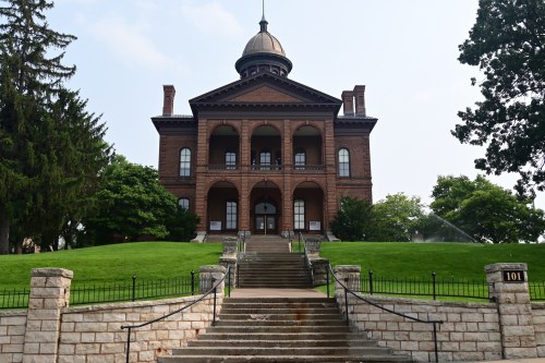 Historic brick building with a dome, flanked by trees, featuring a grand staircase leading to its entrance.