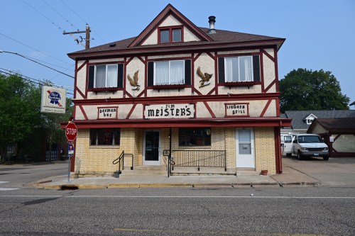 A two-story building with a red and white facade, featuring a bar sign and outdoor seating area.