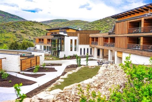 Modern resort buildings with wooden accents, surrounded by green hills and landscaped gardens.