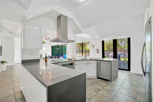 Modern kitchen with white cabinets, gray countertops, and a large island, featuring a stylish hood and open layout.