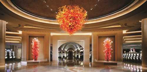 Luxurious casino interior featuring a vibrant glass chandelier and artistic glass installations flanking the entrance.