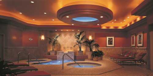 A luxurious spa interior featuring a hot tub, lounge chairs, and decorative plants under warm lighting.