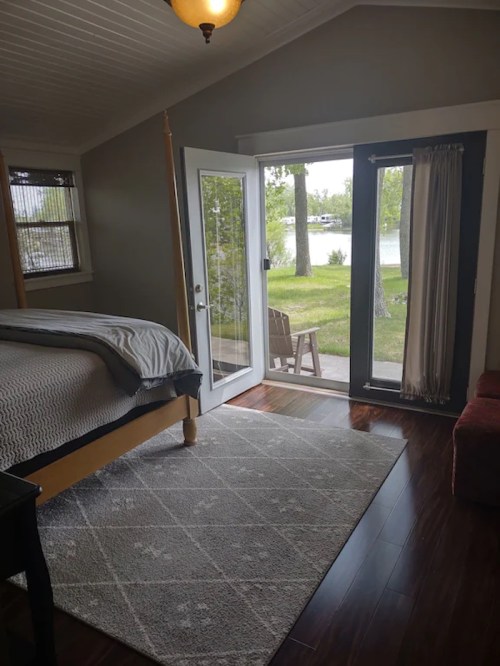 Cozy bedroom with a bed, large windows, and a view of a lake through open doors.