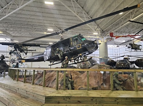 A military helicopter on display in a museum, with soldiers in action poses around it.