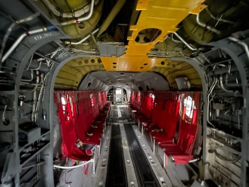 Interior of a military aircraft featuring red seats along the sides and various mechanical components visible.