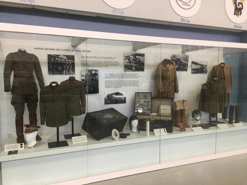 Display case featuring World War I uniforms, weapons, and artifacts, showcasing military history and attire.