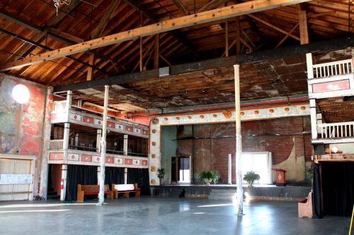 Interior of a spacious, rustic venue with exposed beams, wooden floors, and decorative walls, featuring a stage area.