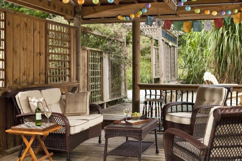 Cozy outdoor seating area with wicker chairs, a small table, and colorful string lights overhead.