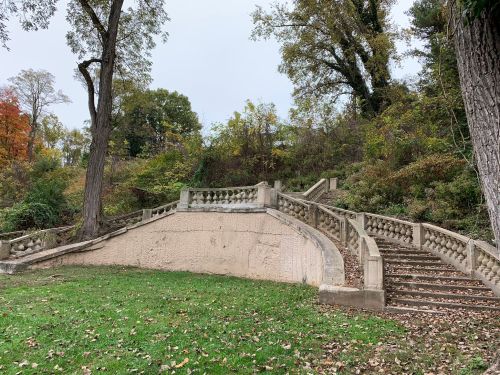 A curved stone staircase leads up a hillside, surrounded by trees and autumn foliage.