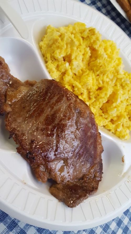 A plate with a grilled steak and a serving of fluffy yellow scrambled eggs.